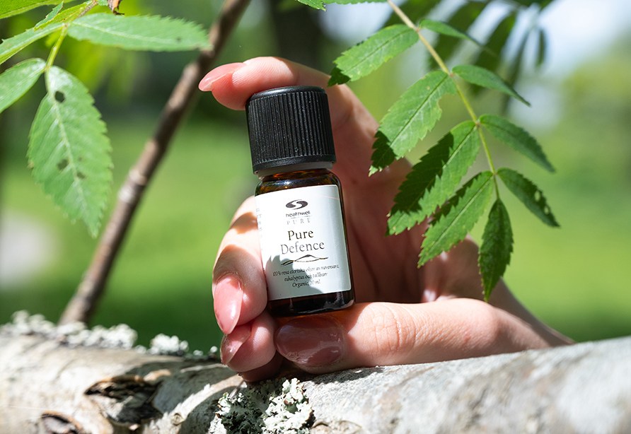 En hnd holder en flaske Healthwell Pure Defence i naturen.